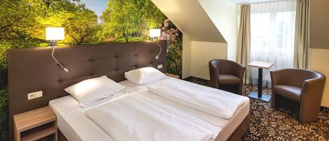 A hotel room with a large bed, a desk, two chairs, and a view of trees through a window.