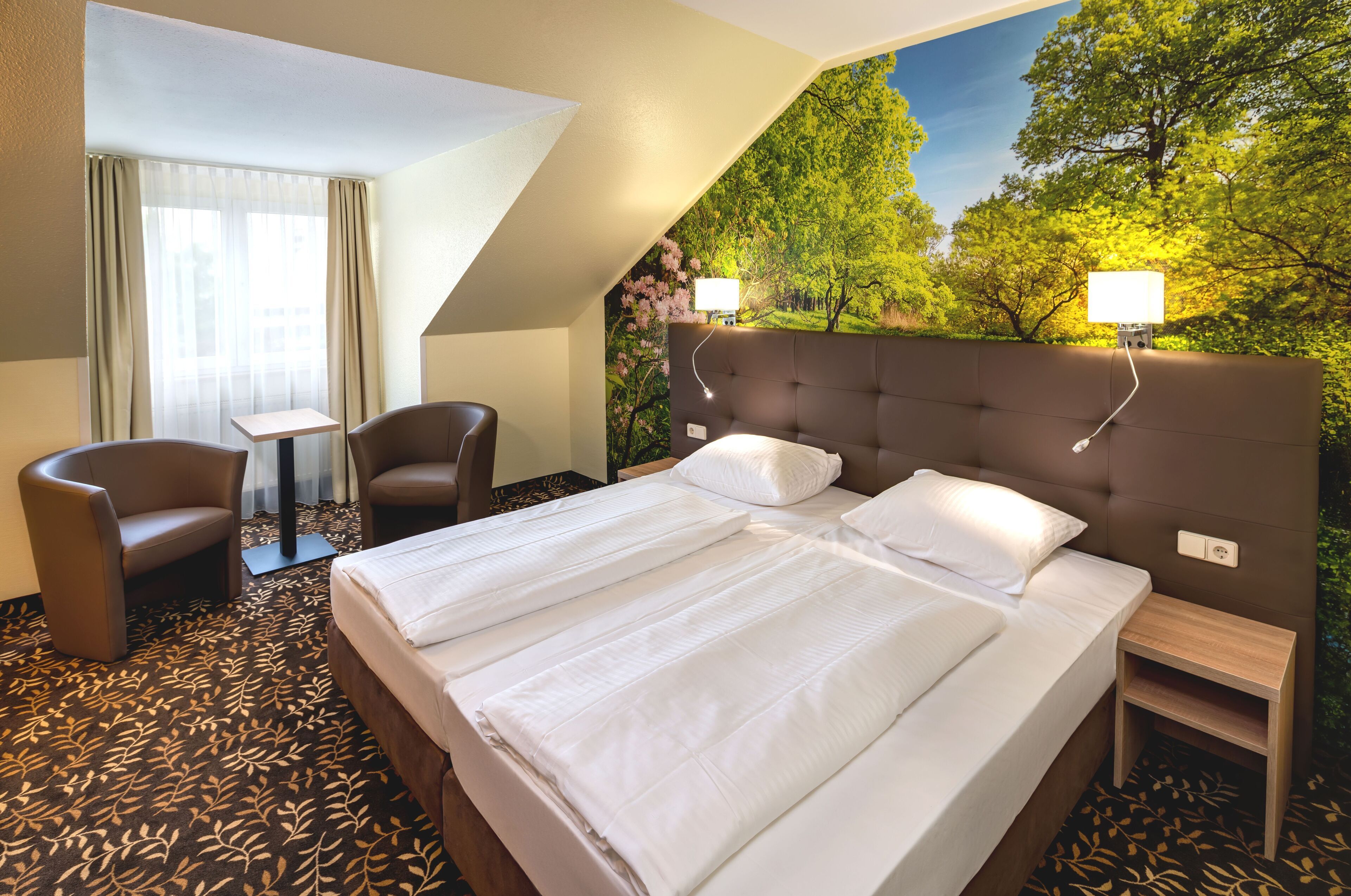 A hotel room with a large bed, two chairs, a small table, and a nightstand.