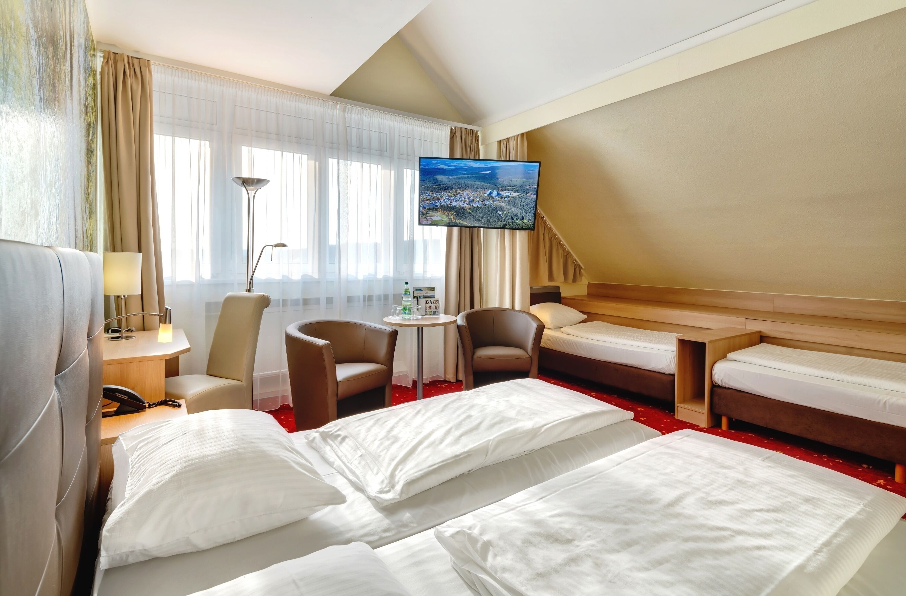 Ein Hotelzimmer mit zwei Betten, einem Fernseher, einem Schreibtisch mit Lampe und einem kleinen Tisch mit Stühlen.