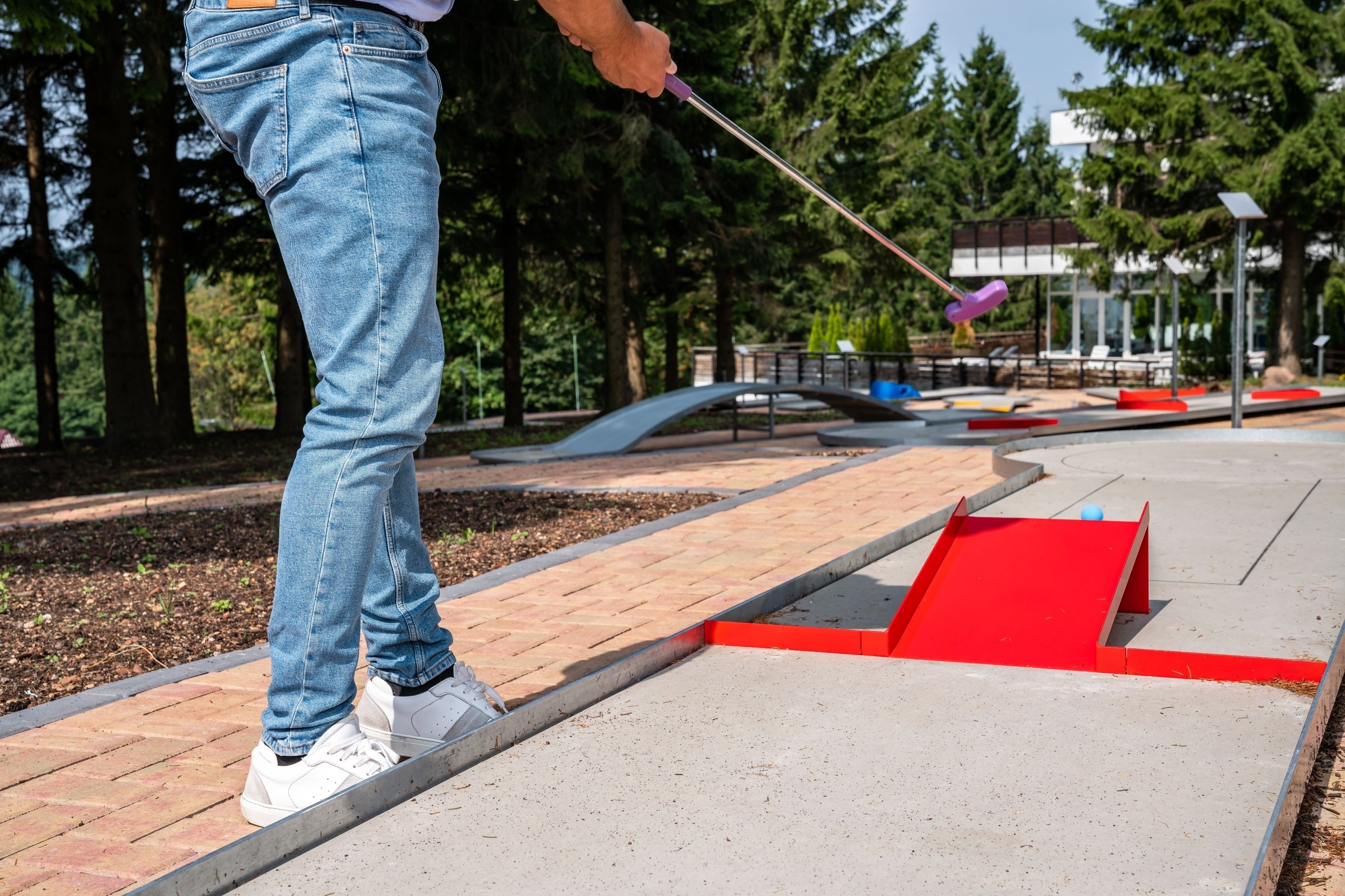 Une personne jouant au golf sur un parcours avec une rampe rouge et un pont en arrière-plan.