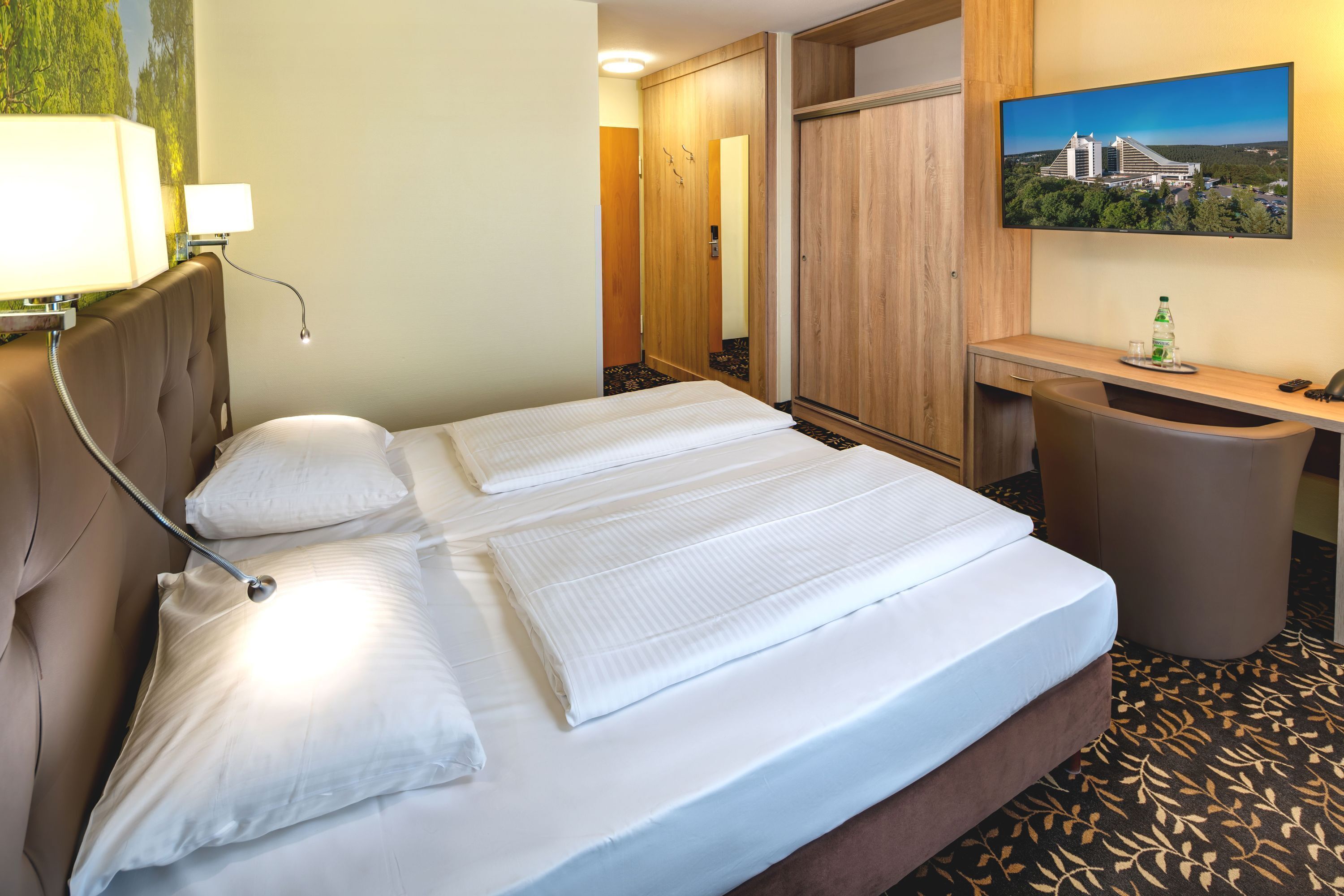 Hotellihuone, jossa on sänky, työpöytä, tuoli, peili ja televisio.