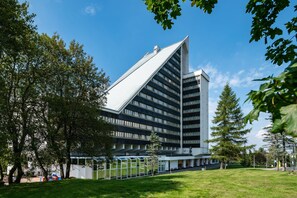 Un bâtiment moderne doté d’un toit triangulaire original, entouré d’arbres et d’une zone verdoyante.