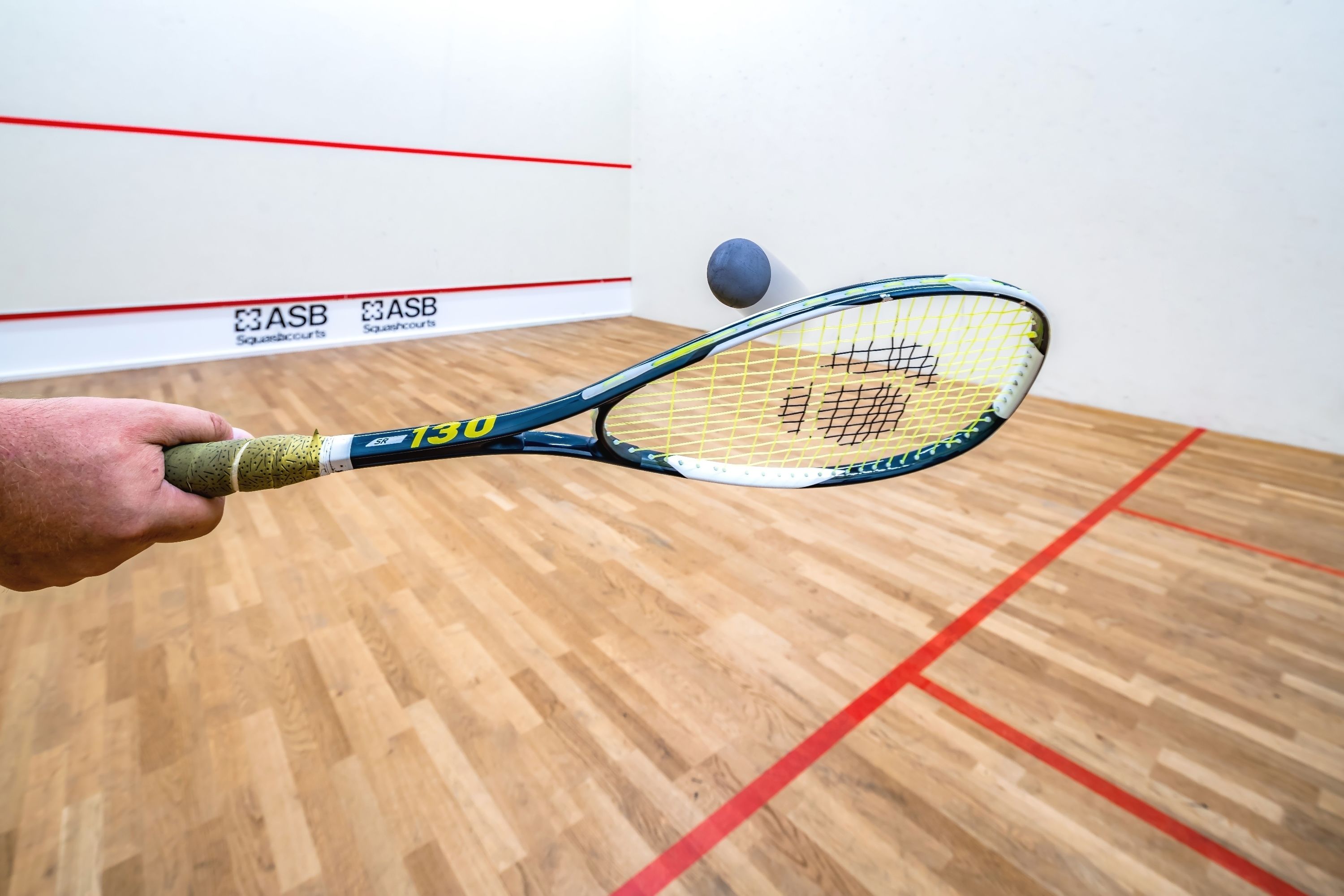 A squash court with wooden flooring and red boundary lines.