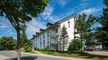 A multi-story residential building with balconies, surrounded by greenery and a clear sky.
