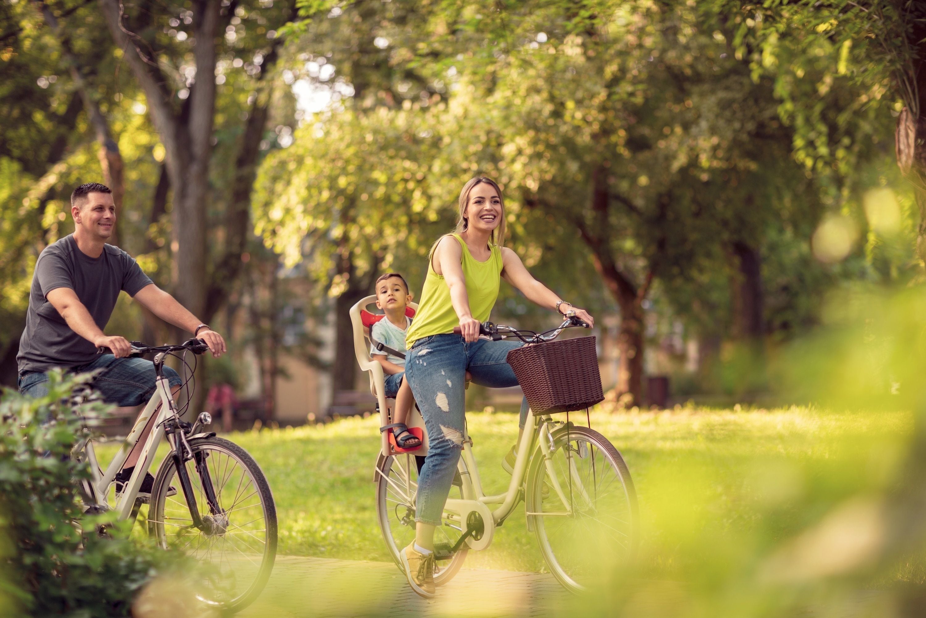 Una familia pasea en bicicleta por un parque con árboles y césped.
