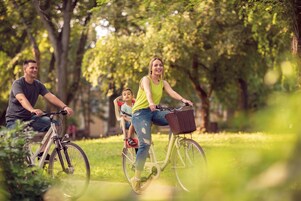 Una familia pasea en bicicleta por un parque con árboles y césped.