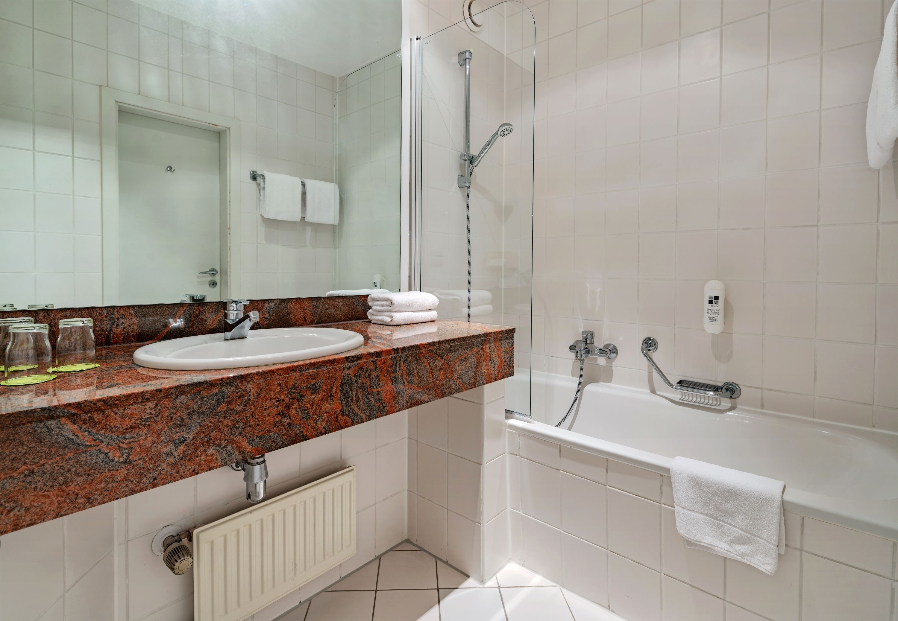 A modern bathroom with a granite countertop sink, a glass-enclosed shower, and a white bathtub.