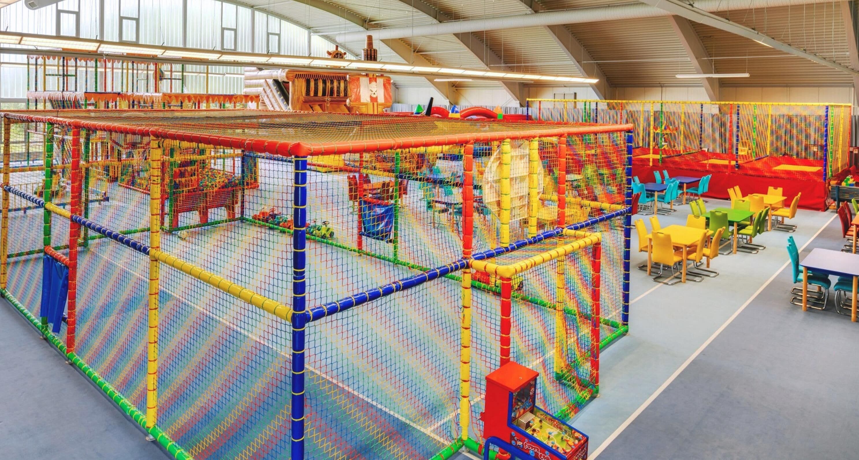 Ein überdachter Spielbereich mit einem Netzspielgerät, Tischen und Stühlen.