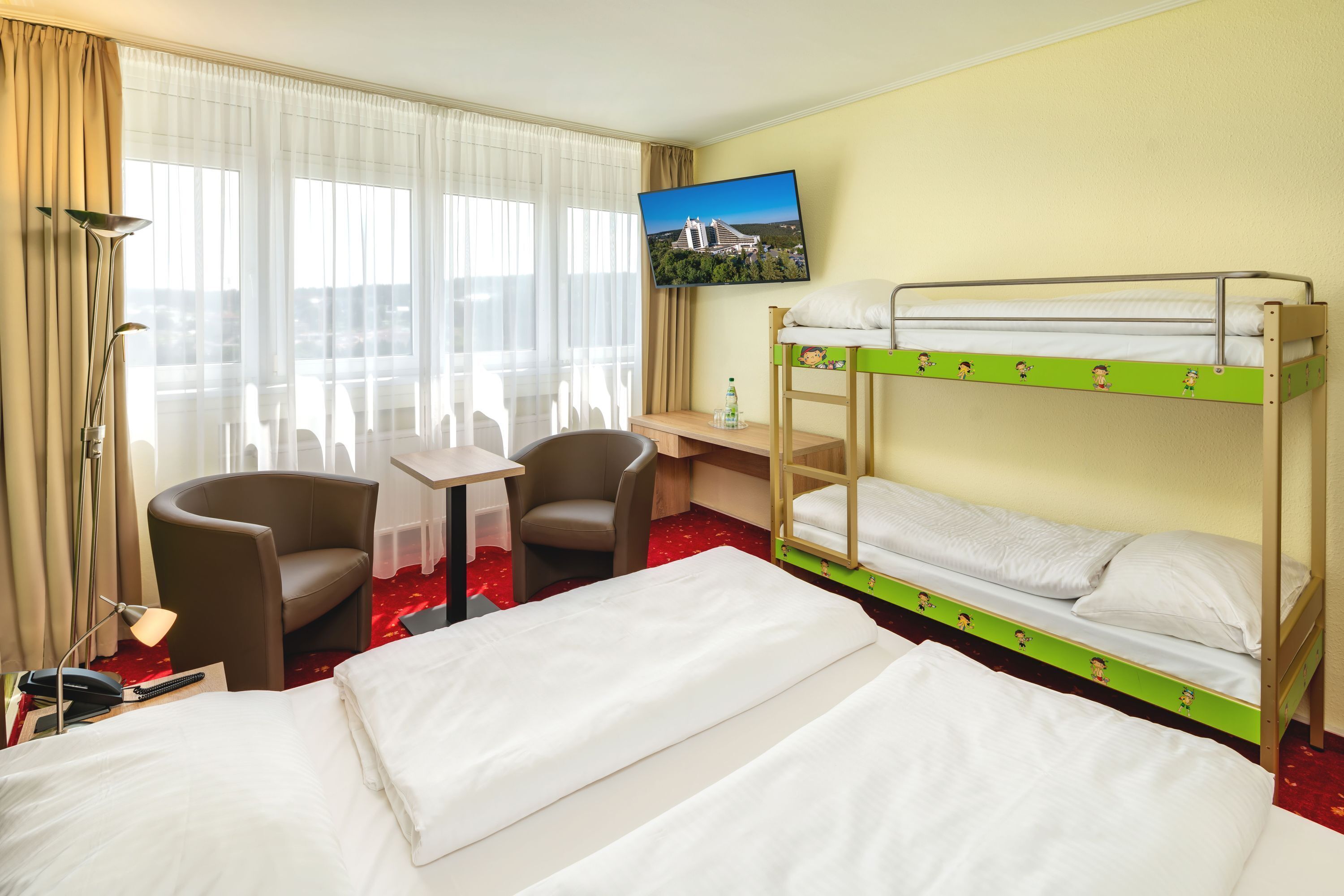 Ein Hotelzimmer mit zwei Betten, einem Fernseher, einem Schreibtisch und zwei Sesseln.