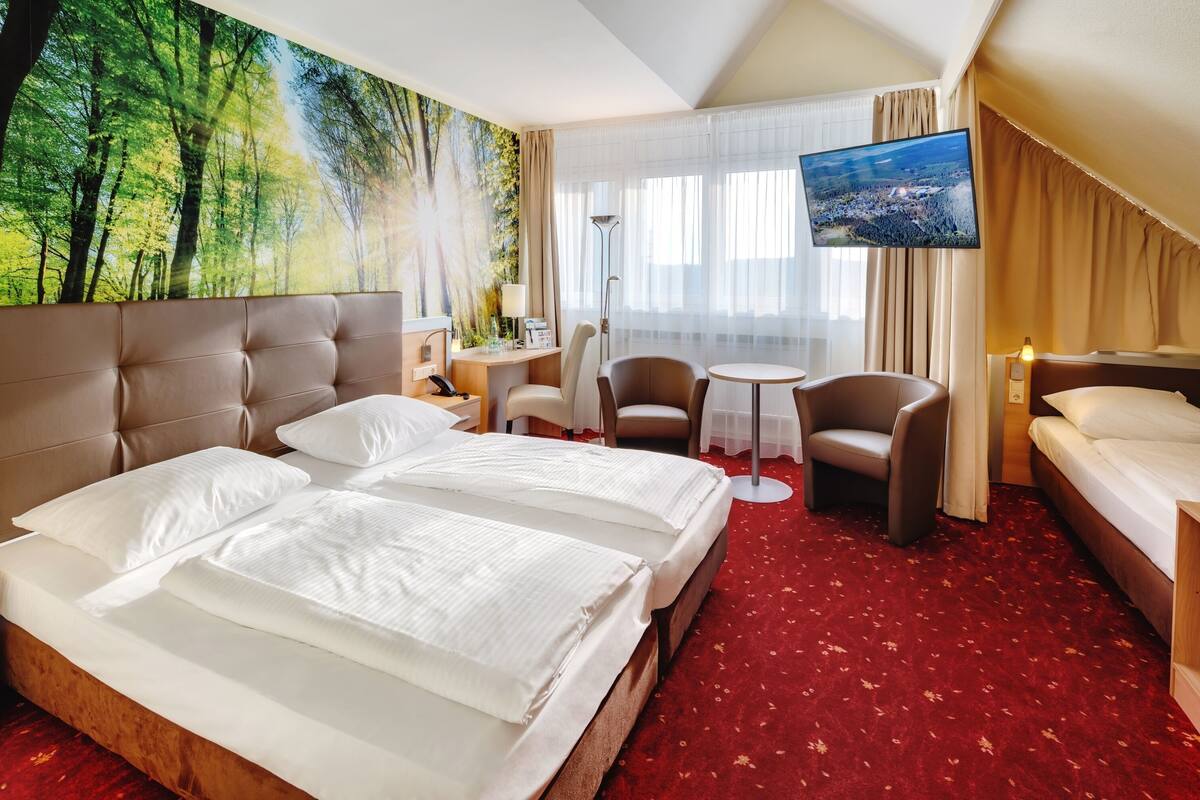 A hotel room with a large bed, a desk, a chair, a small table, and a TV.