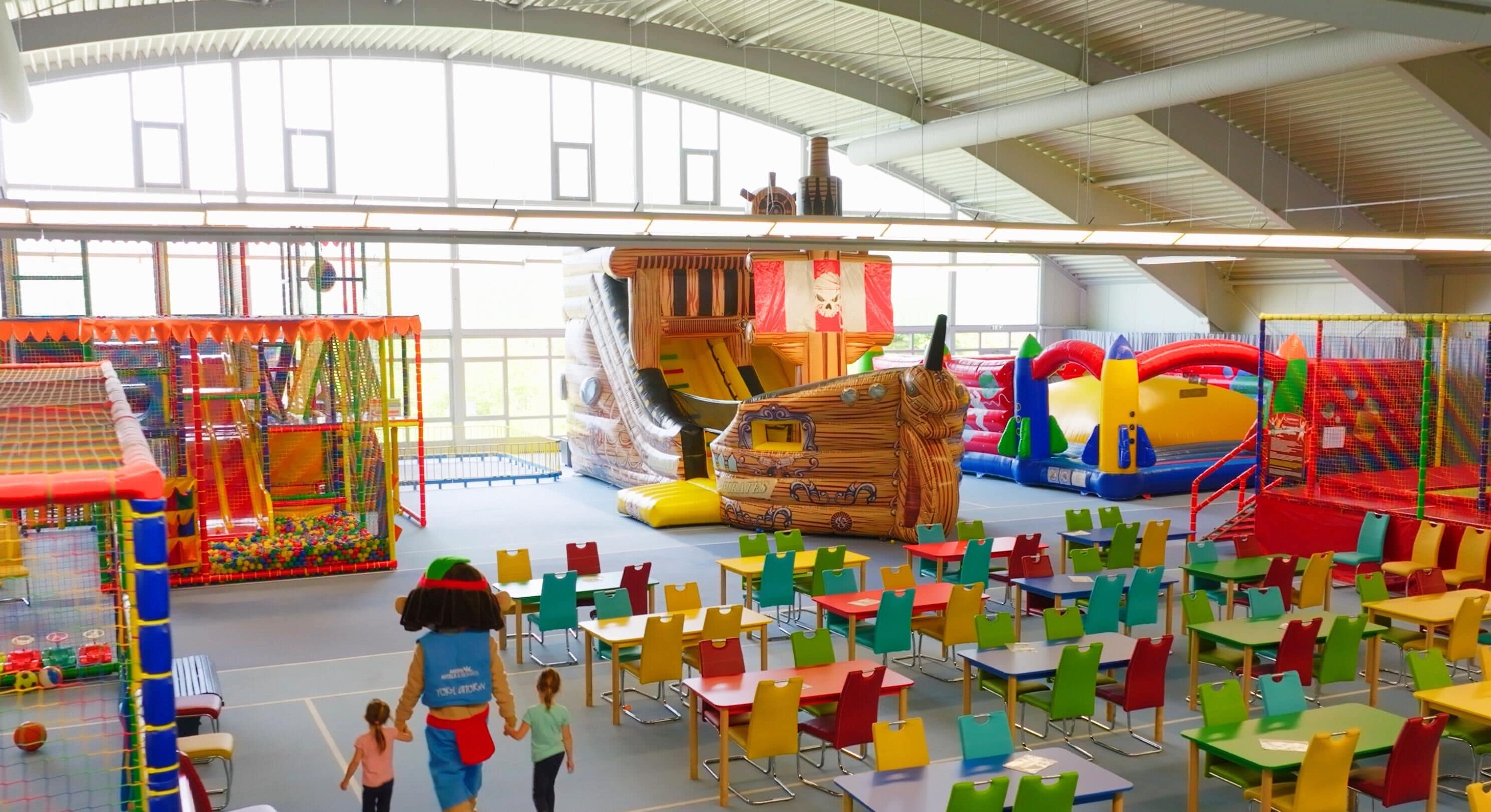Un espacio de juego interior con estructuras de juego coloridas, mesas y sillas dispuestas para niños.