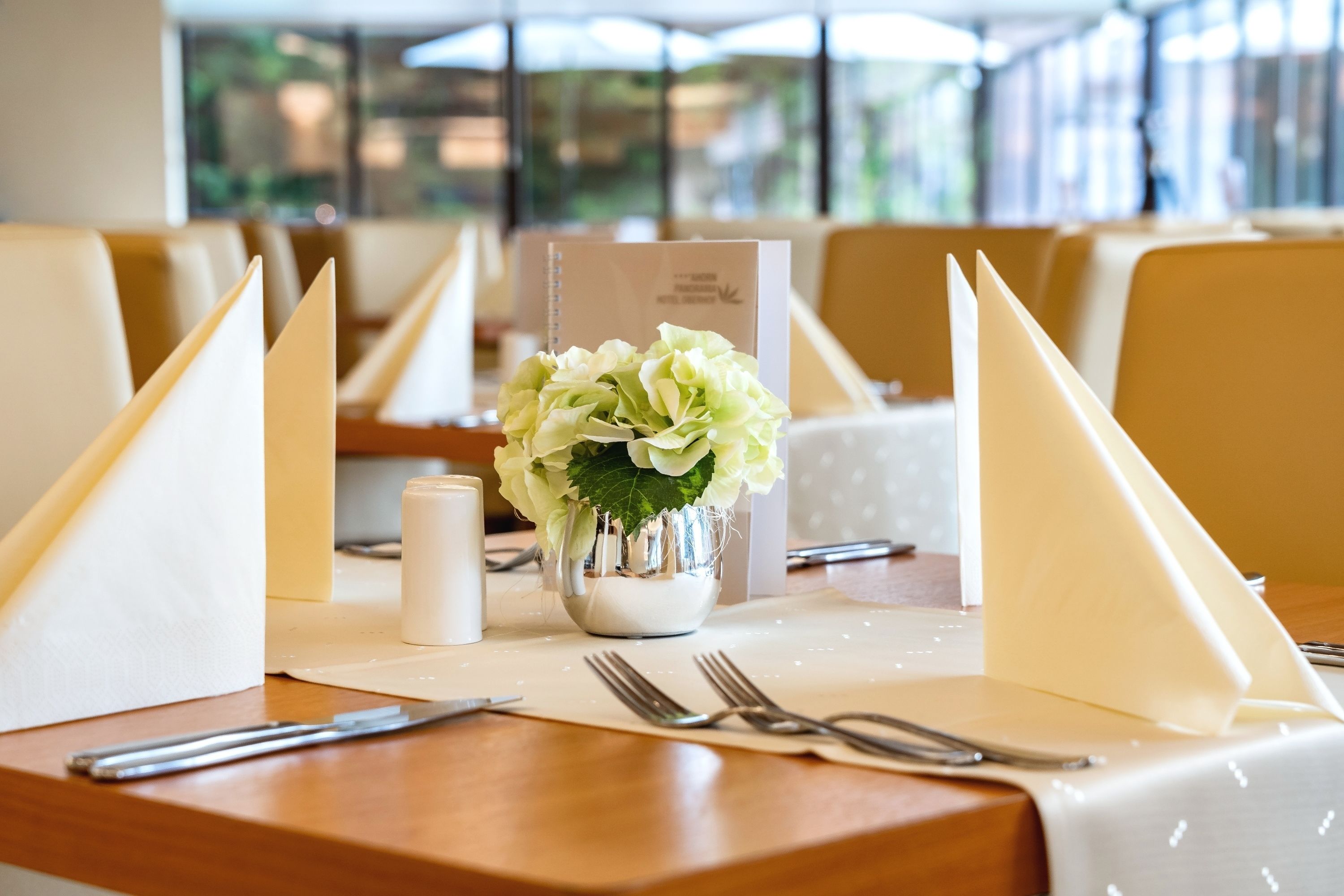 A dining table set with a white tablecloth, a small vase with white flowers, and folded napkins.