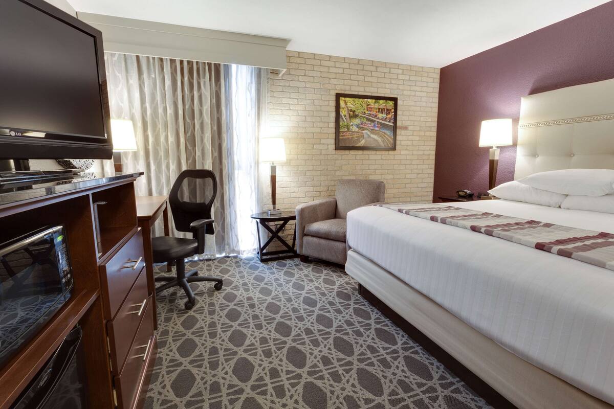 A hotel room with a bed, a TV, a desk with a computer, a chair, and a lamp.