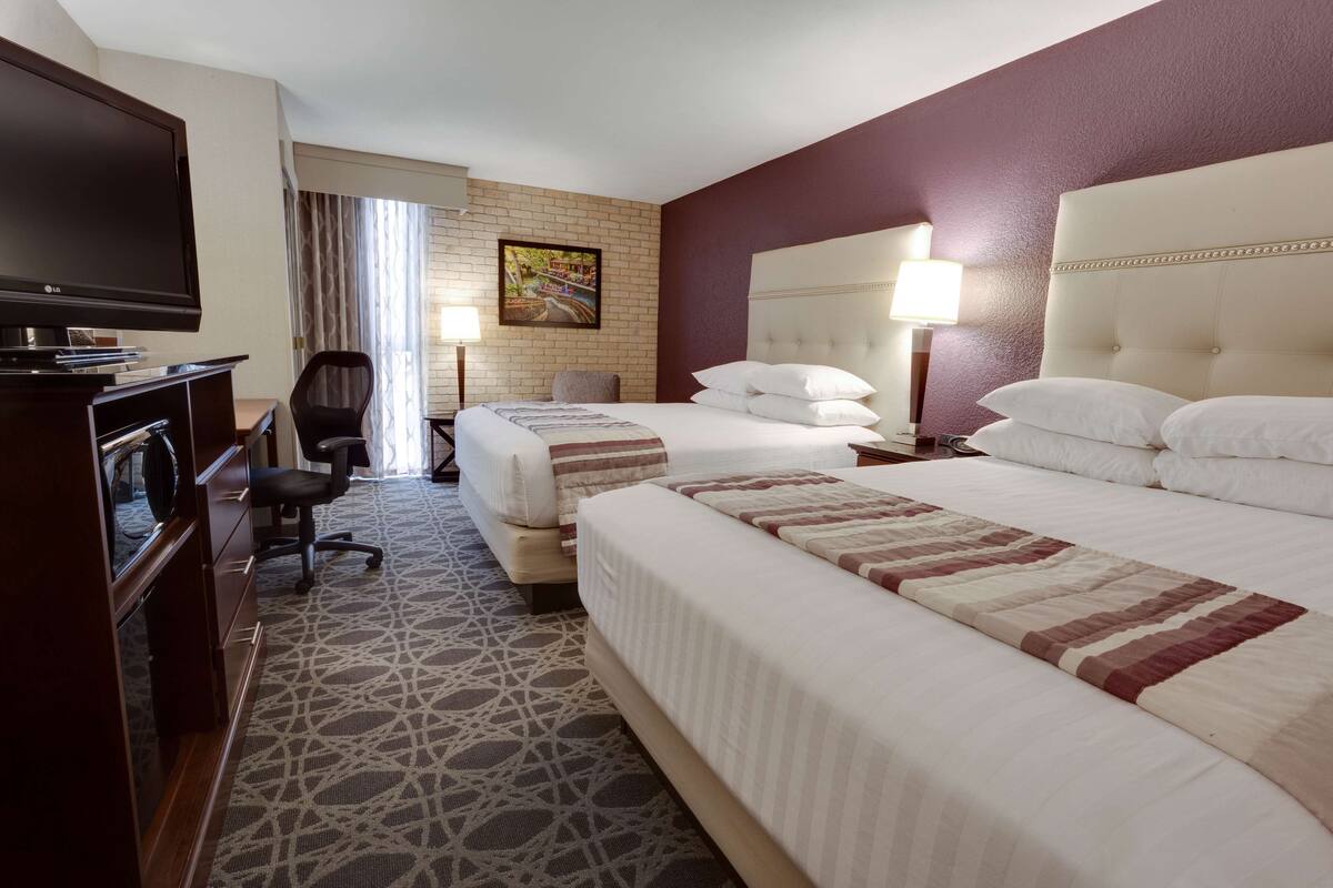 A hotel room with two beds, a desk with a television, a chair, and a patterned carpet.