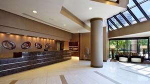 A modern hotel lobby with a marble reception desk, decorative wall art, a seating area with a view of the outdoors, and a large window. - Embassy Suites by Hilton Crystal City National Airport (Arlington)