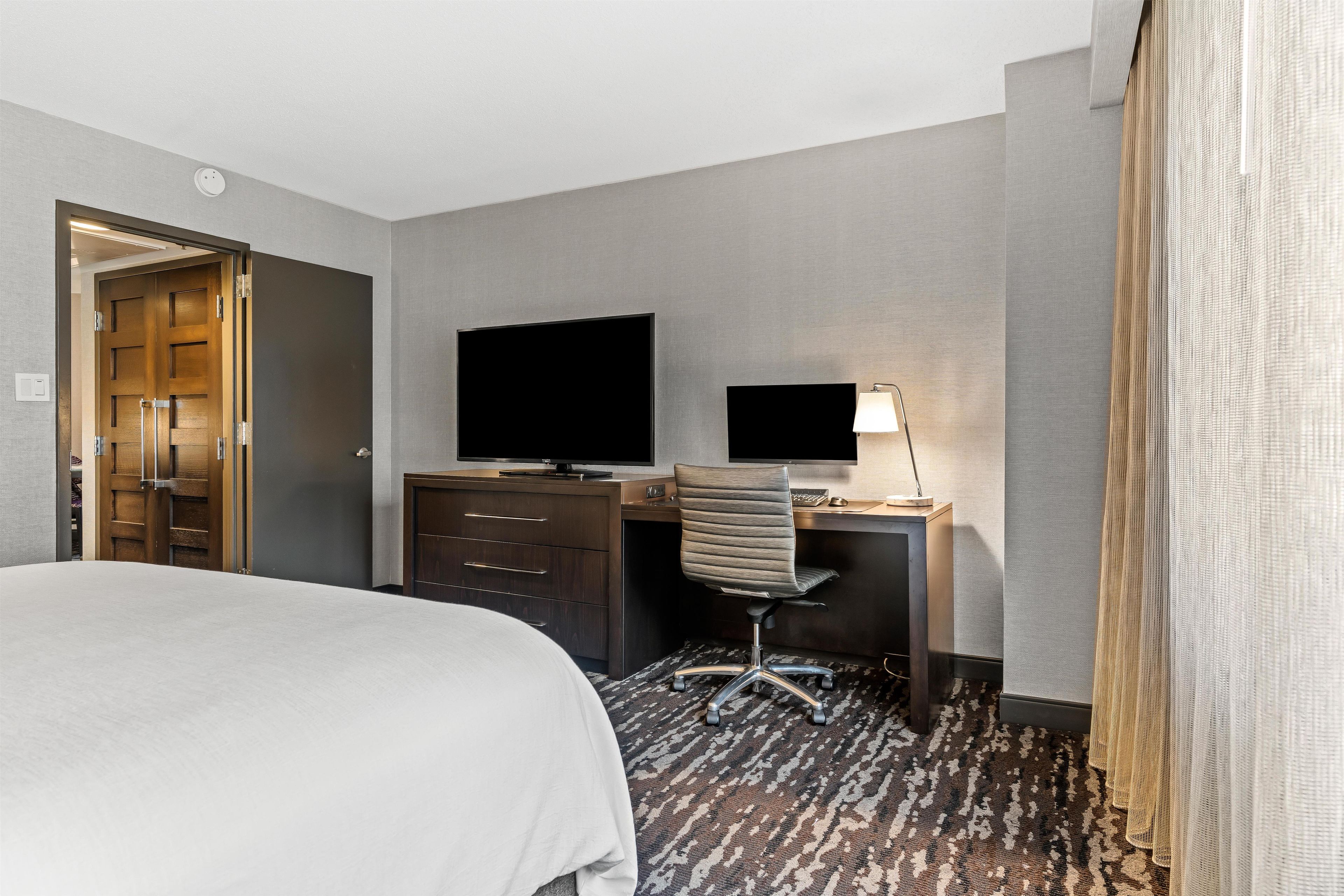 Una habitación de hotel con cama, escritorio con computadora, televisor y una silla.