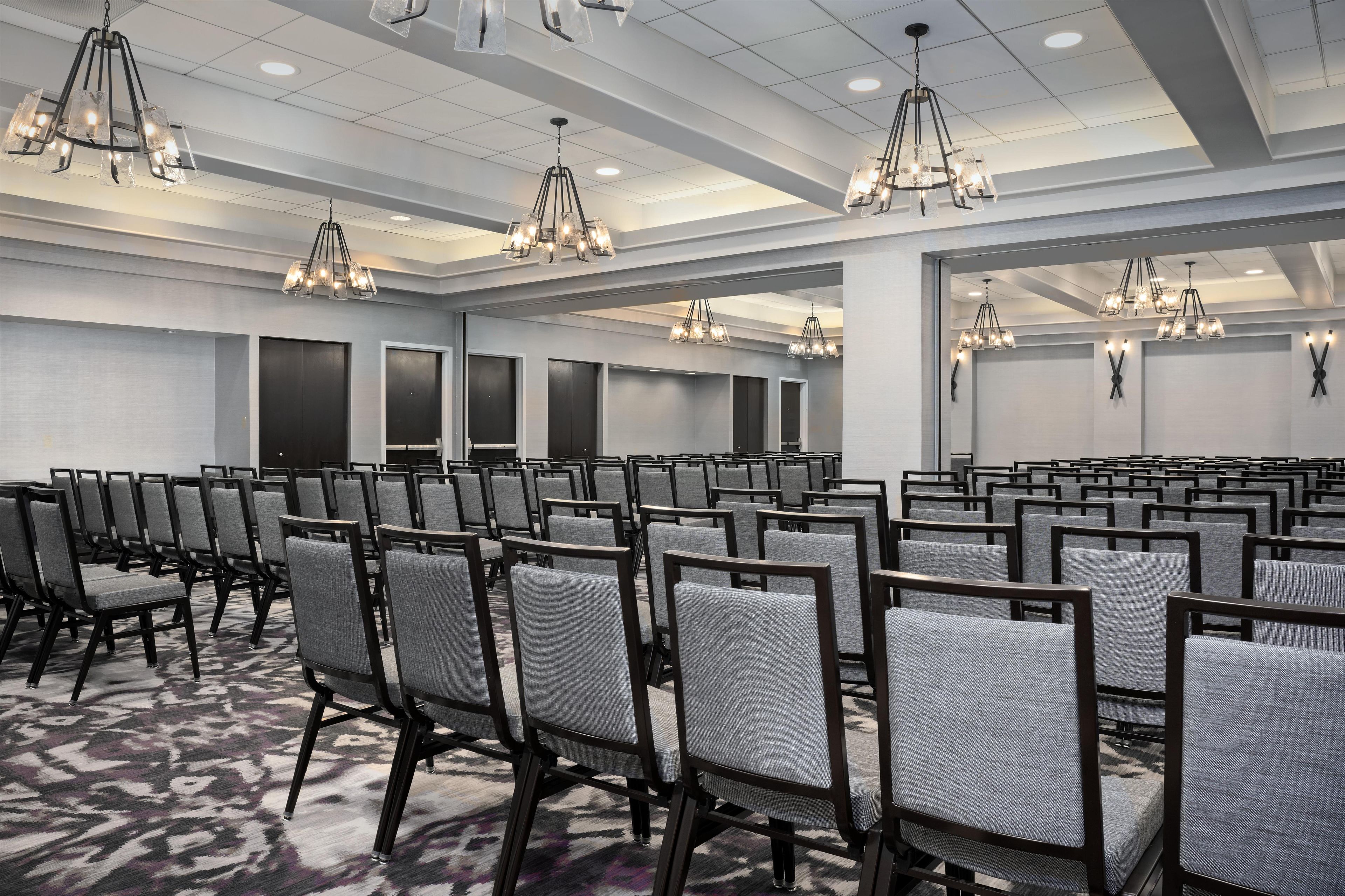 A conference room with rows of chairs, multiple chandeliers, and a patterned carpet.