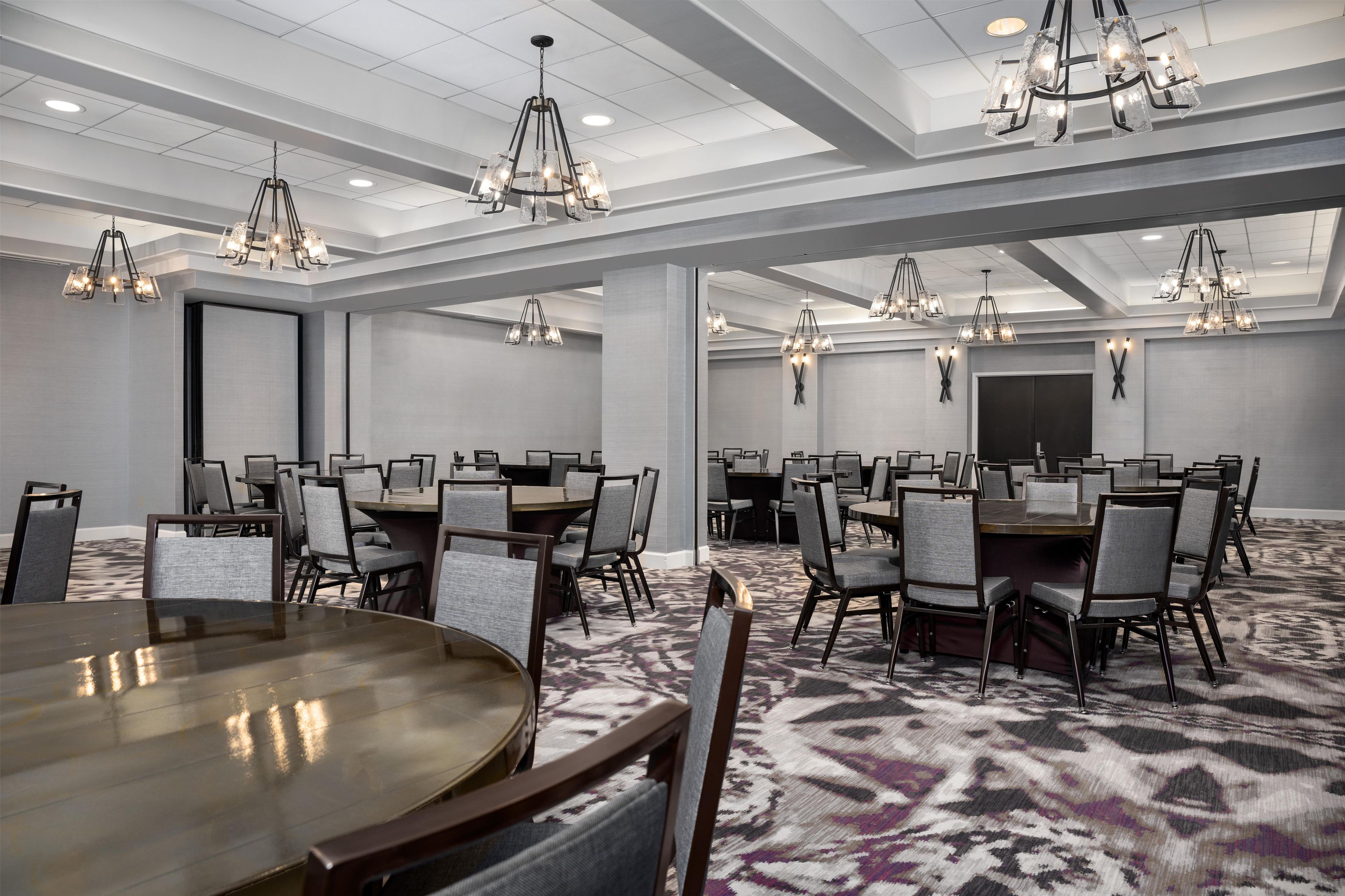 A conference room with multiple tables and chairs, chandeliers, and a patterned carpet.