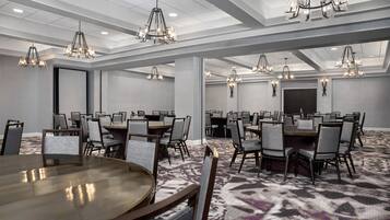 A conference room with multiple tables and chairs, chandeliers, and a patterned carpet.