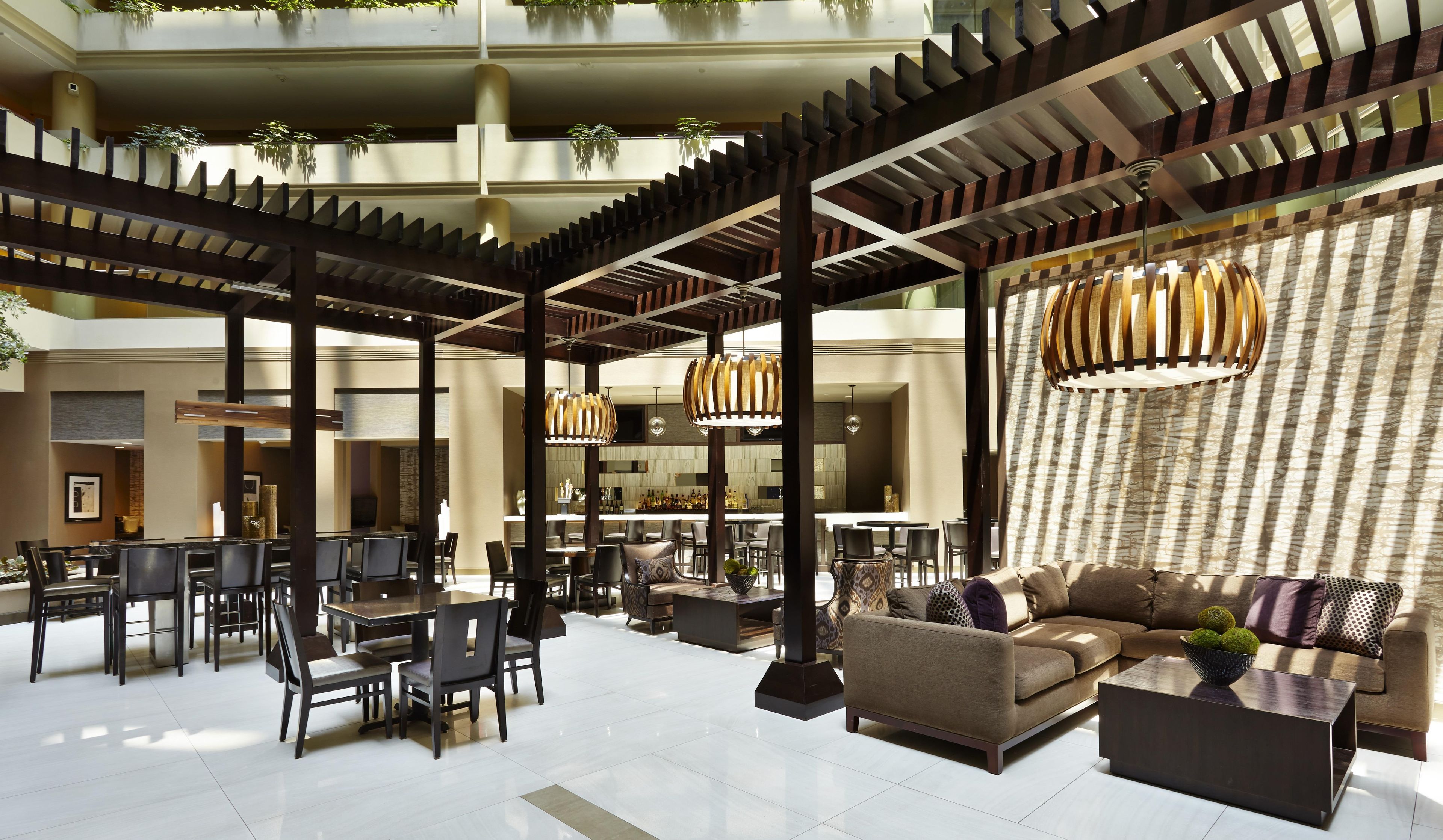 A spacious lobby with a modern design, featuring a central seating area with sofas and chairs, a bar area, and a high ceiling with structural beams.
