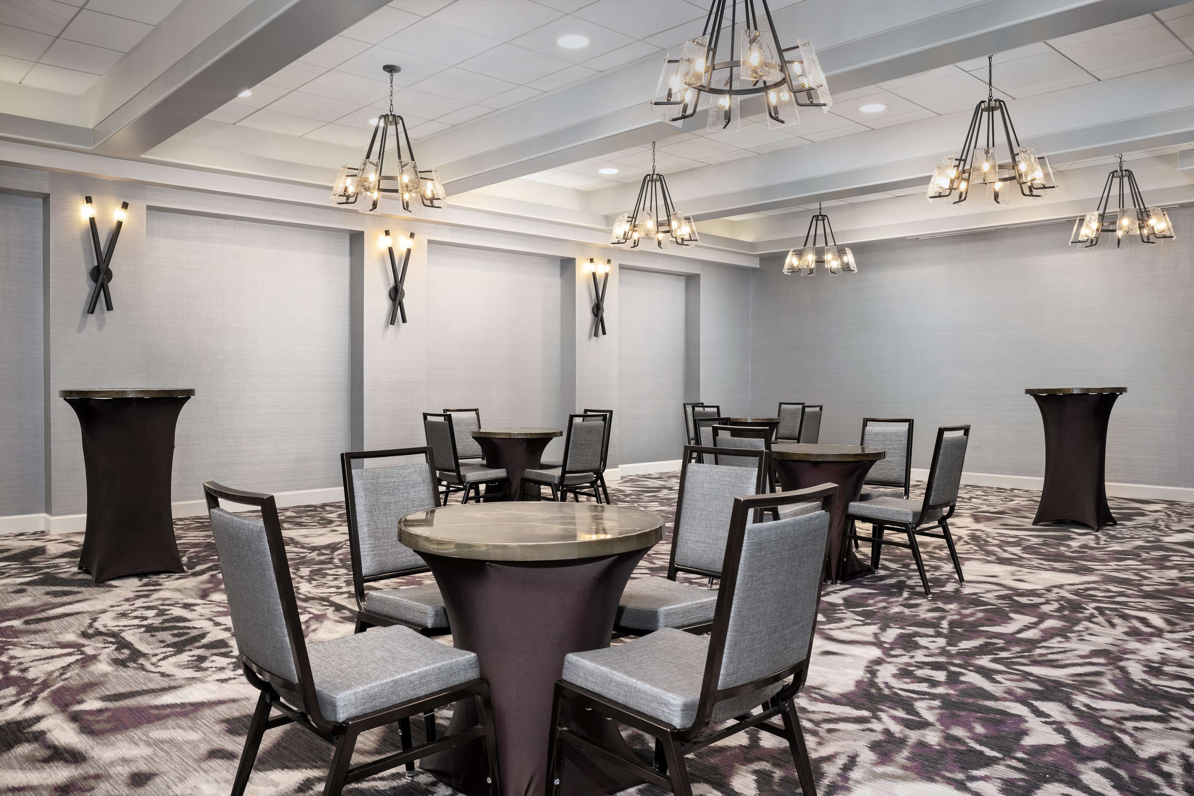 Un salón de conferencias con mesas y sillas redondas, candelabros y una alfombra estampada.