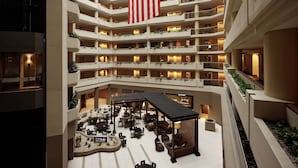 A multi-level hotel atrium with a large American flag, multiple balconies, and a central food and craft bar area. - Embassy Suites by Hilton Crystal City National Airport (Arlington)