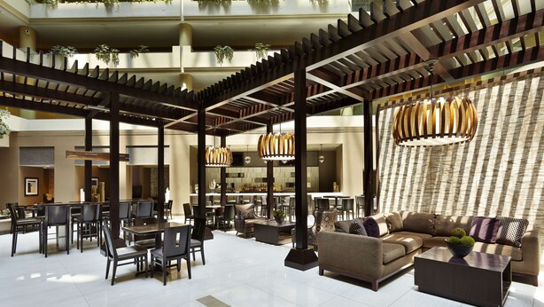 A spacious lobby with a modern design, featuring a central seating area with sofas and chairs, a bar area with a counter, and a high ceiling with exposed beams and hanging lights. - Embassy Suites by Hilton Crystal City National Airport (Arlington)