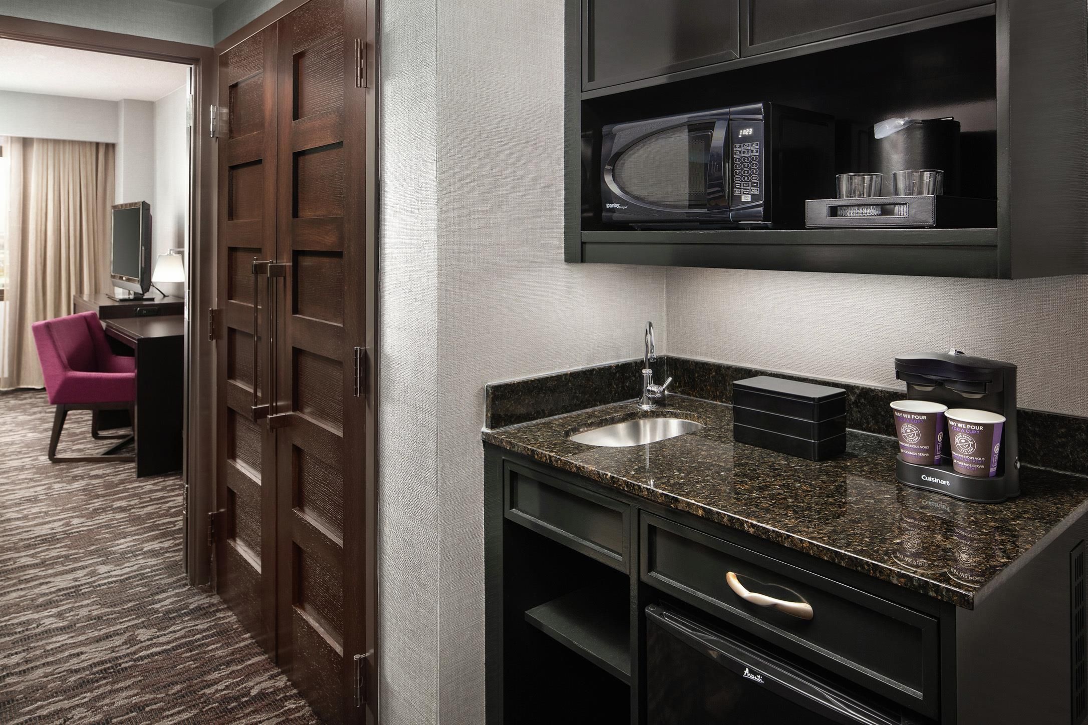 A hotel room with a kitchenette, including a microwave, coffee maker, and a sink.