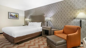 A hotel room with a large bed, a nightstand with a lamp, an orange armchair, and a patterned carpet.