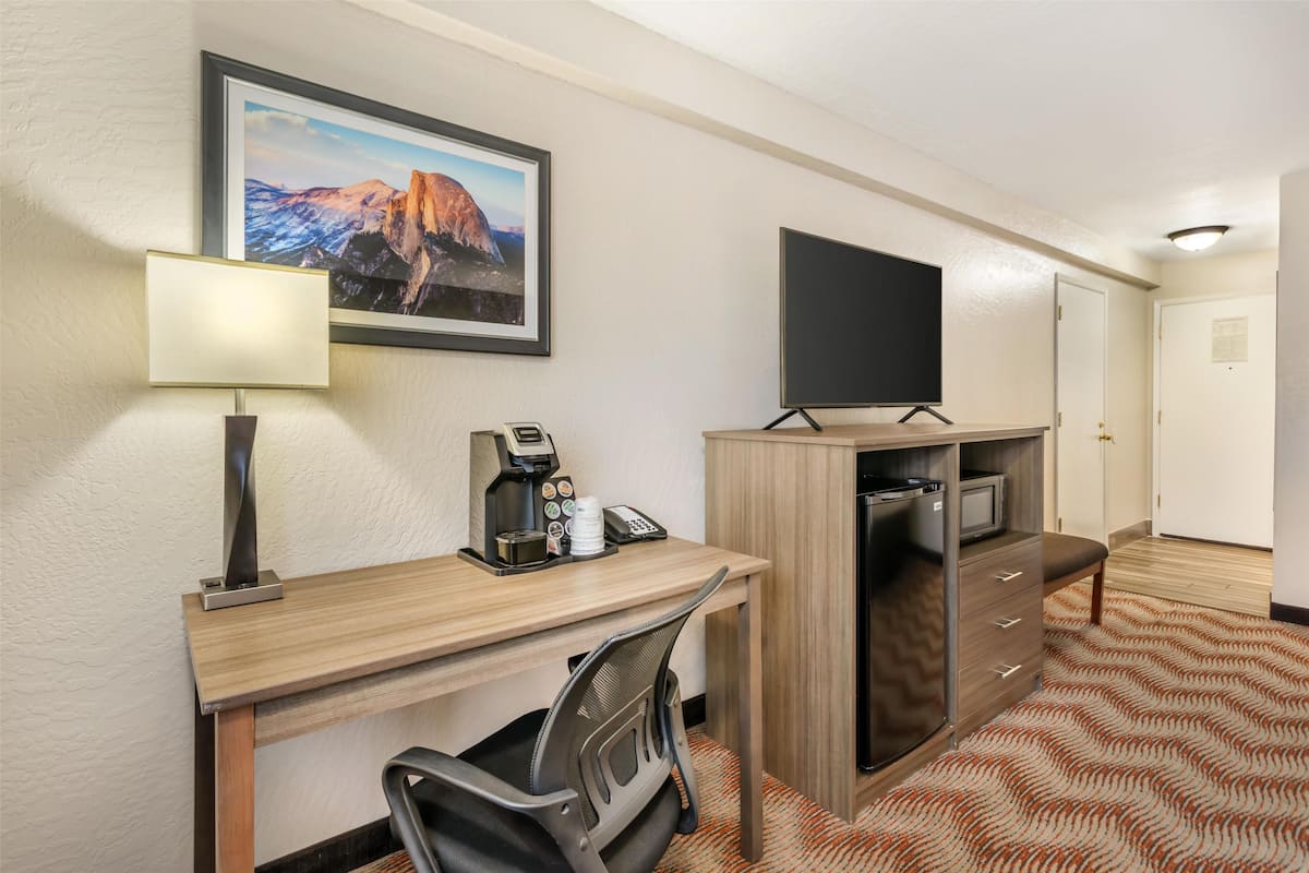 Una habitación de hotel con escritorio, silla, televisor, cafetera y un cuadro en la pared.