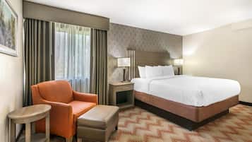 A hotel room with a large bed, a chair, a small table, and a nightstand with lamps.