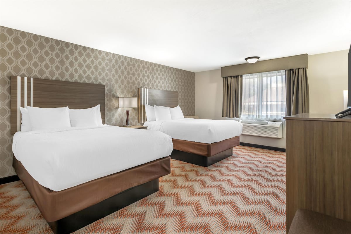 Habitación de hotel con dos camas, un escritorio y una ventana con cortinas.