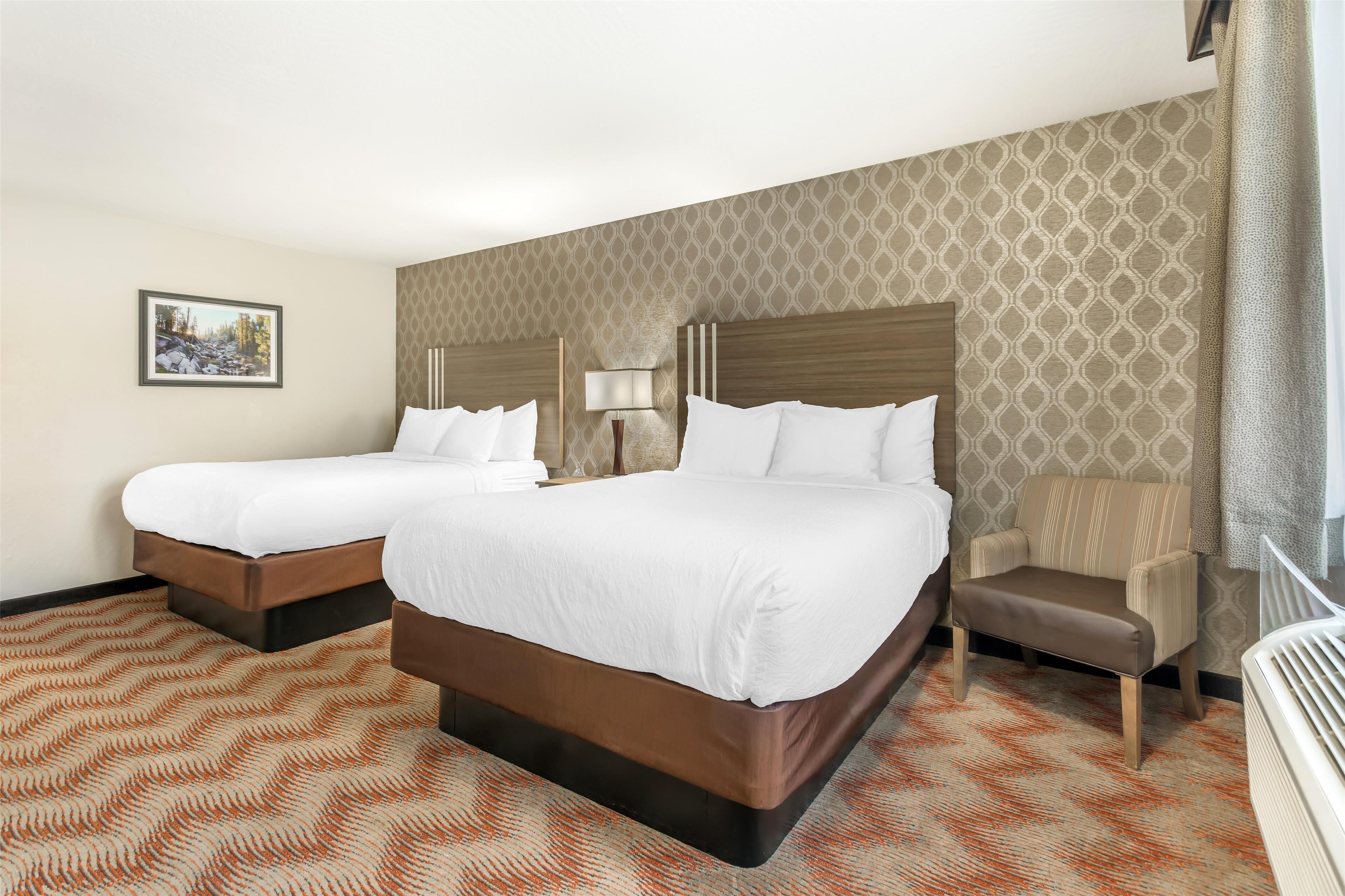 A hotel room with two beds, a chair, a lamp, and a patterned carpet.