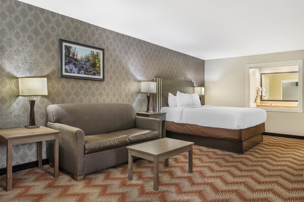 A hotel room with a bed, a sofa, a small table, and a nightstand with lamps.