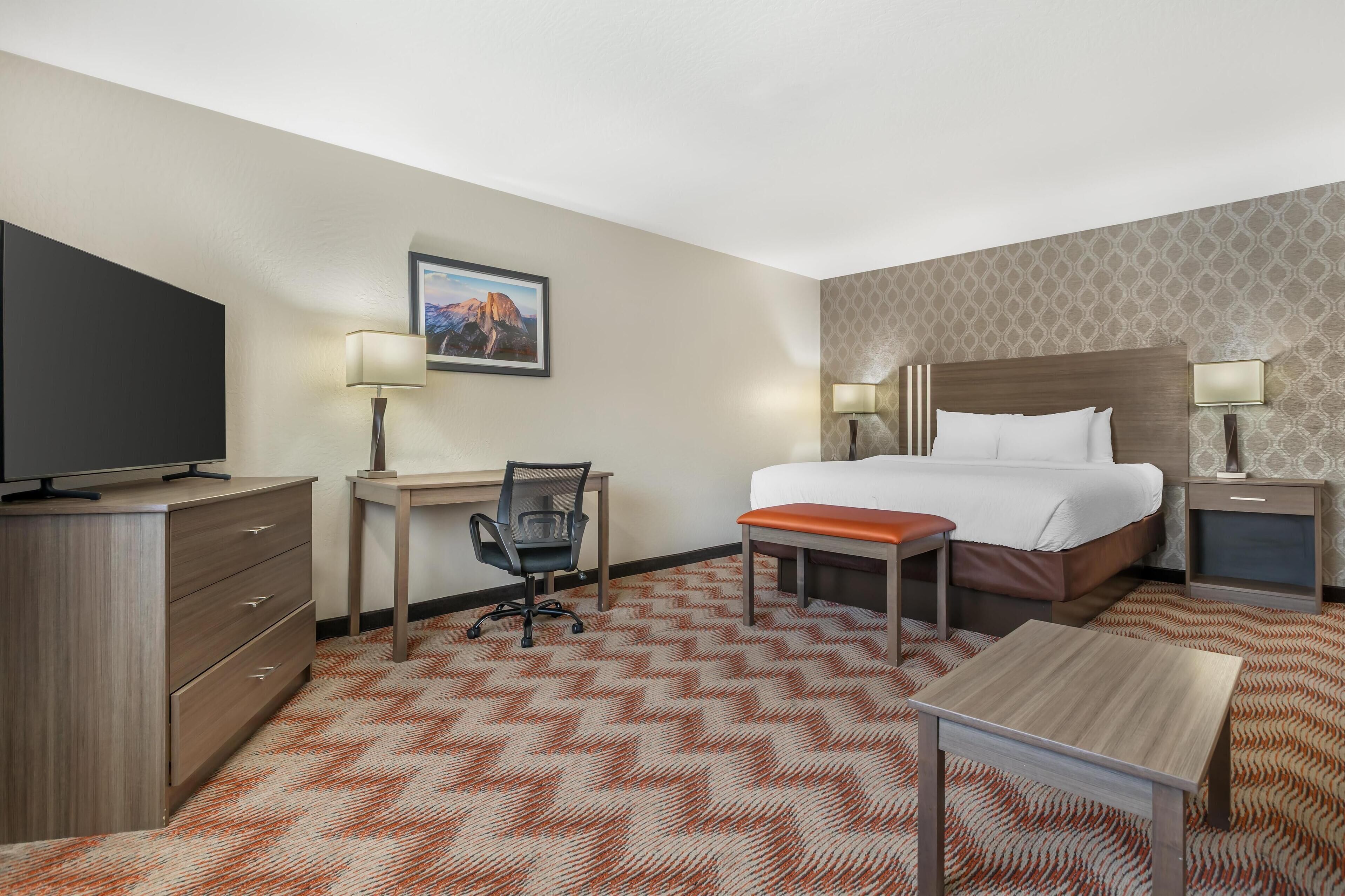 A hotel room with a bed, desk, chair, TV, and two bedside tables with lamps.