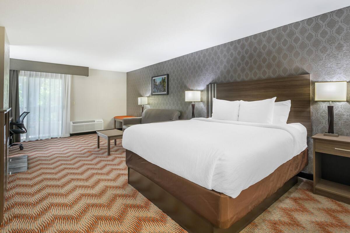 Habitación de hotel con una cama grande, dos mesitas de noche con lámparas, un escritorio, una silla y una ventana con cortinas.