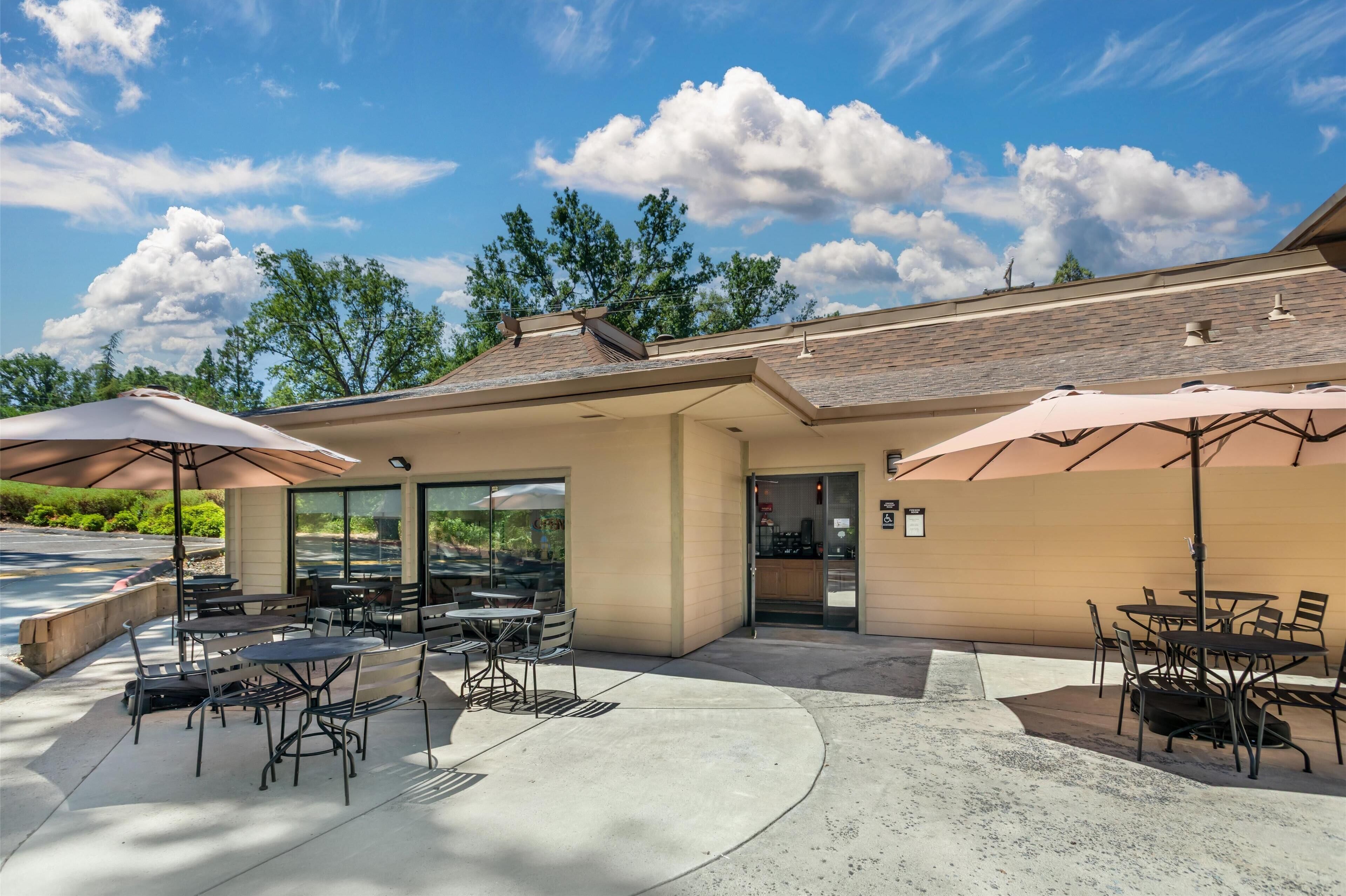 An outdoor patio area with tables and chairs, large umbrellas, and a building entrance.