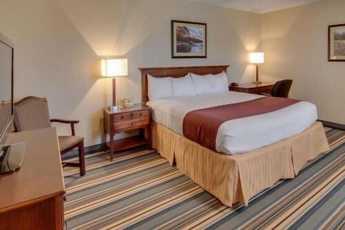 A hotel room with a bed, two bedside tables, a chair, a desk, and a carpeted floor.