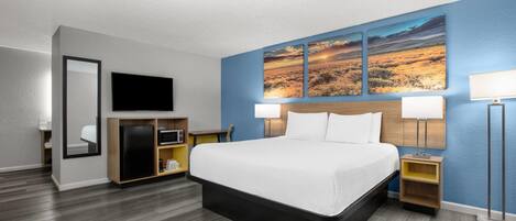 A hotel room with a large bed, a flat-screen TV, a desk with a computer, a microwave, and a refrigerator.