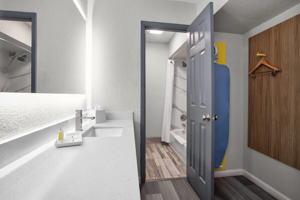 Un baño con encimera blanca, espejo, ducha y puerta de madera.