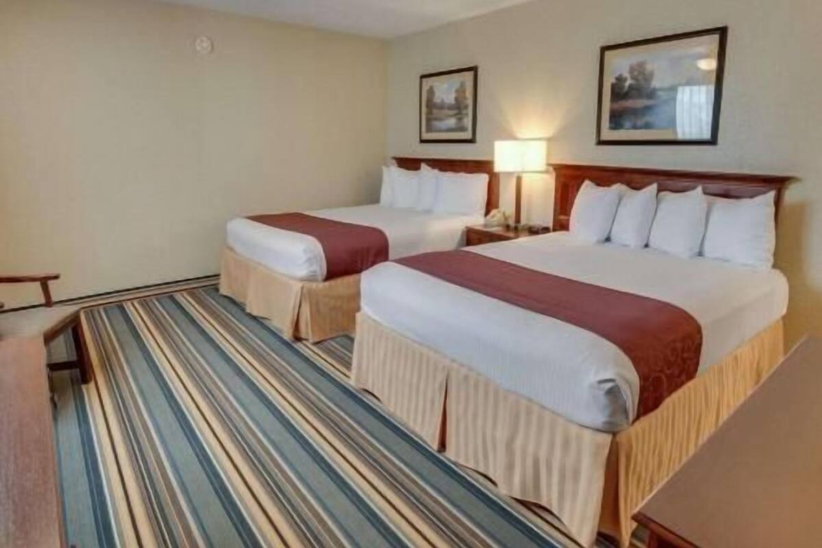 A hotel room with two beds, a striped carpet, and two framed pictures on the wall.