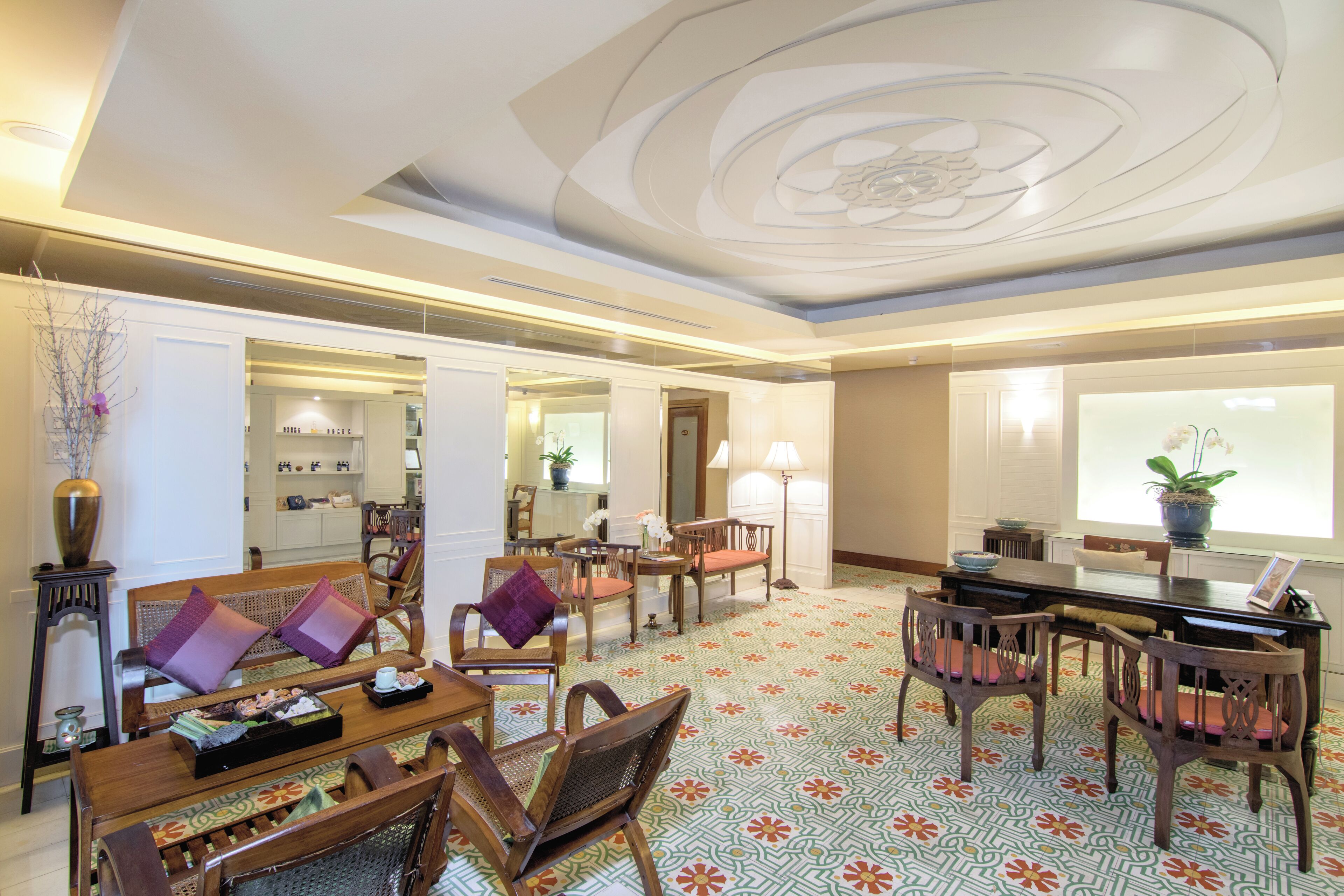 A spacious hotel lobby with a traditional design, featuring a central dining area with wooden furniture and a patterned floor.