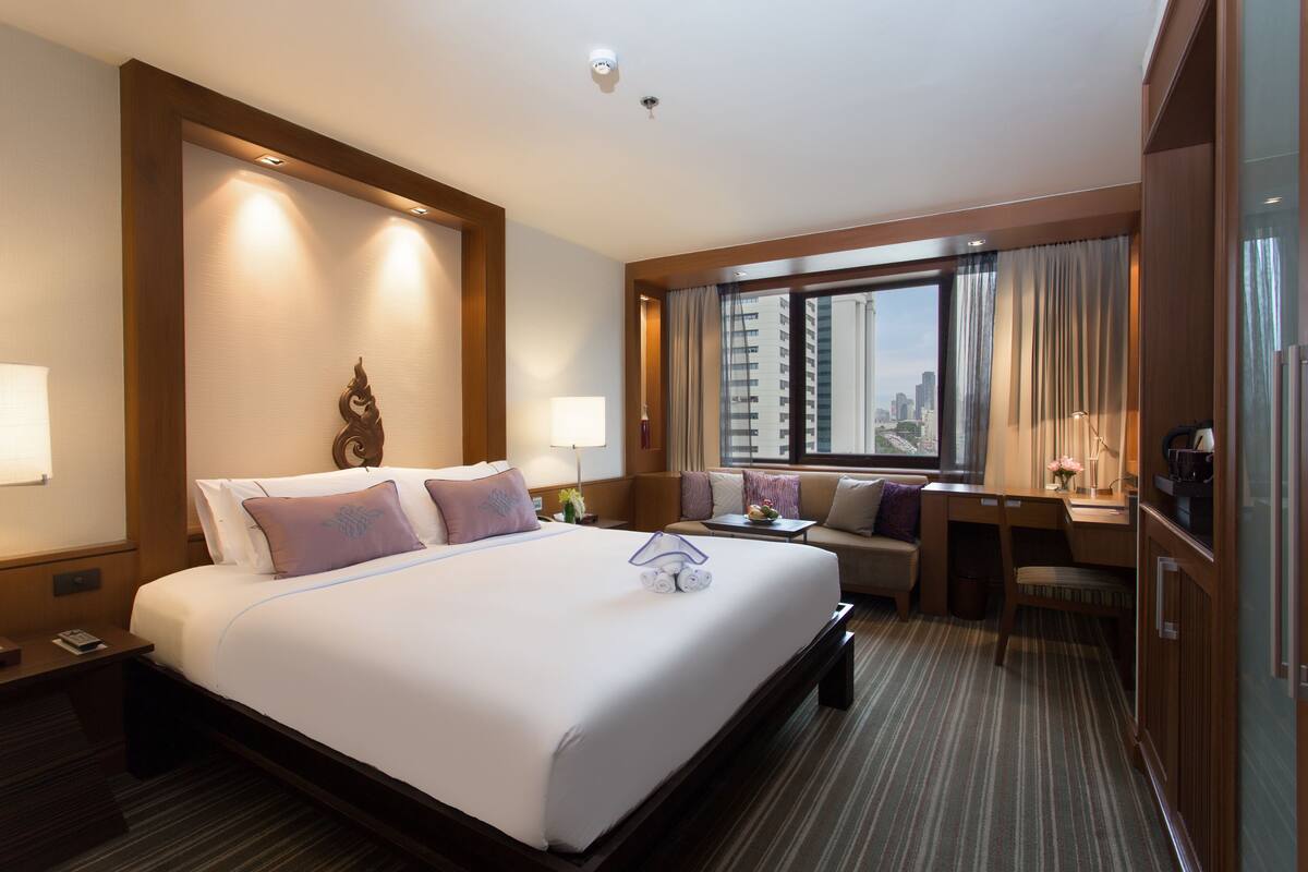 A hotel room with a large bed, a desk, a sofa, and a view of the city.