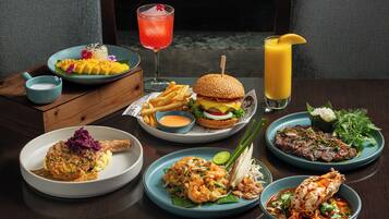 A variety of dishes including a burger, seafood, and a salad, arranged on a wooden table with a view of a window in the background.