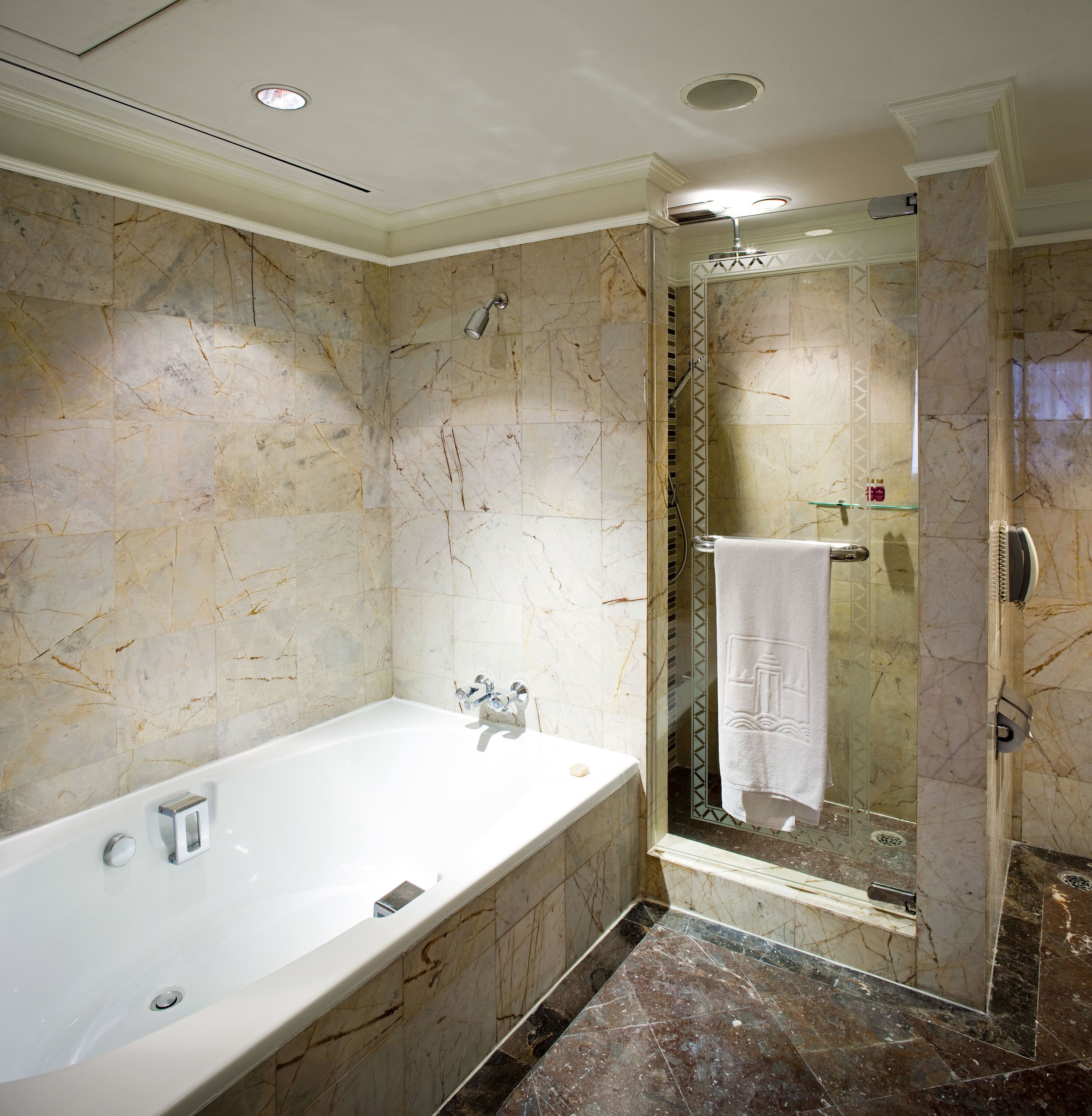 Un baño moderno con una bañera grande, una ducha con mampara de cristal y paredes de mármol.