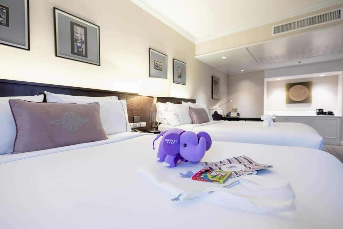 A hotel room with two beds, a nightstand, a lamp, and framed pictures on the wall.