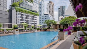 A rooftop pool with lounge chairs and potted plants, surrounded by high-rise buildings. - The Sukosol (Bangkok)