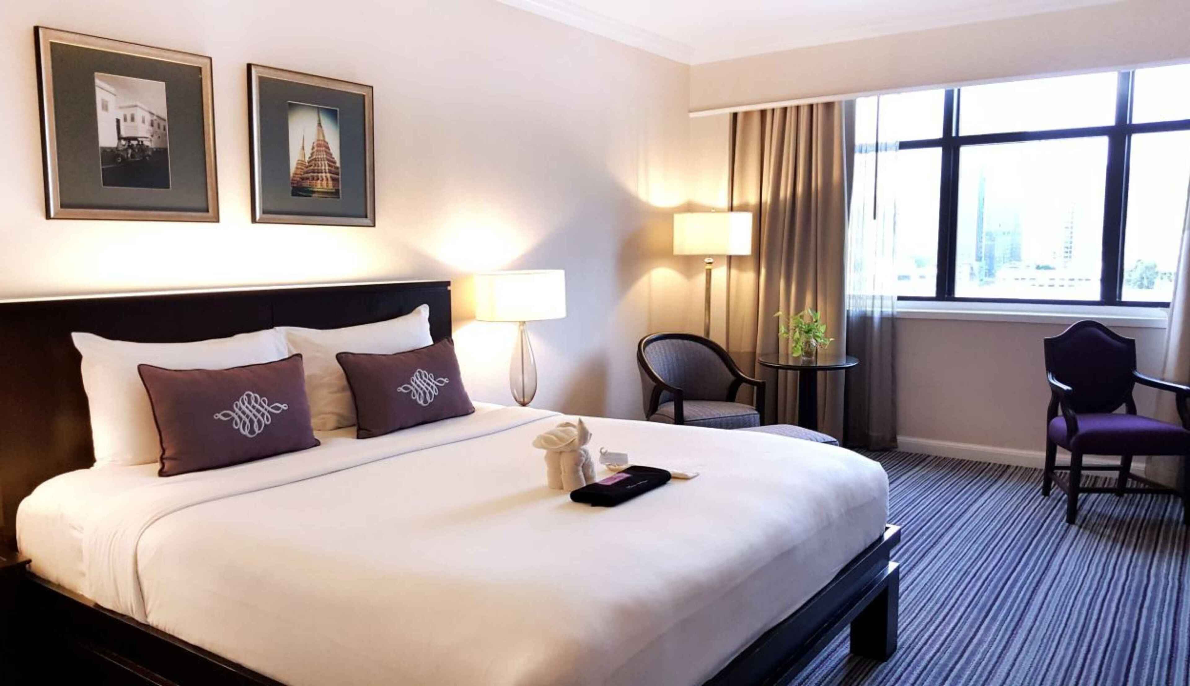 A hotel room with a large bed, two framed pictures on the wall, a desk with a chair, and a window with a view.