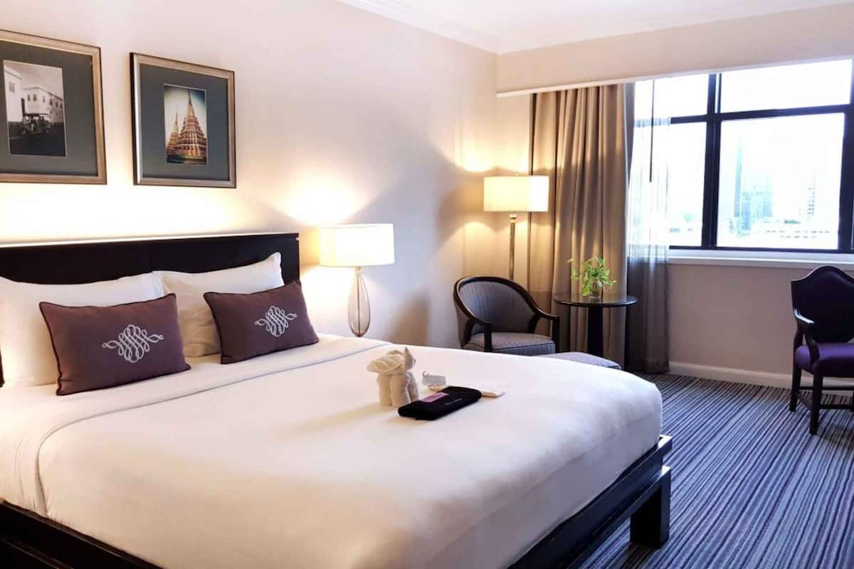 A hotel room with a large bed, two framed pictures on the wall, a desk with a chair, and a window with a view.