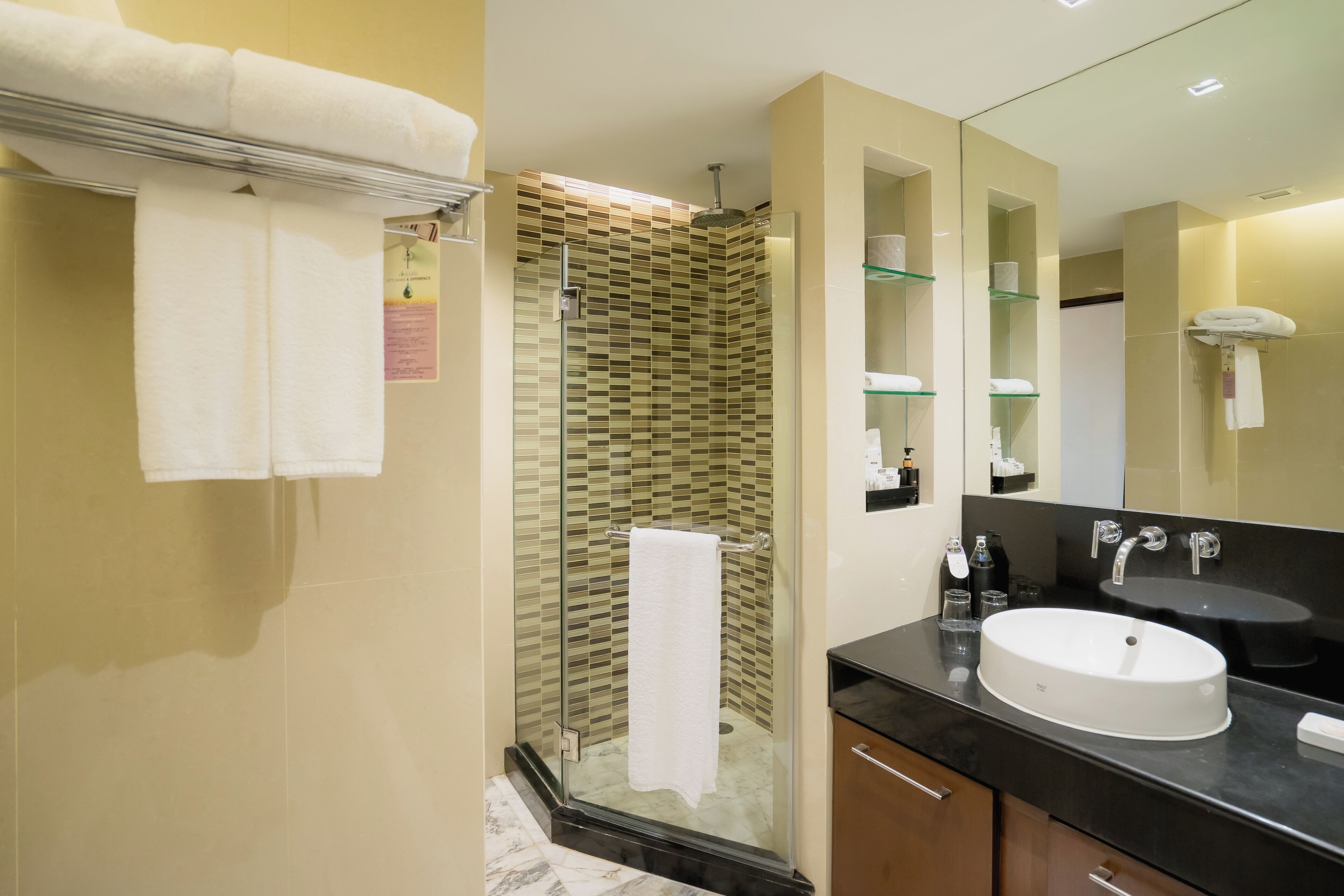 Une salle de bain moderne avec une douche à parois de verre, un grand miroir et un plan de toilette noir avec un lavabo blanc.